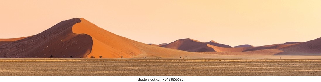 Desert landscape at sunrise, wilderness scene of Namibia. Red sand dunes in Namib desert. Wide panorama of Sossusvlei valley in a soft light for travel banner, warm tints of sand. - Powered by Shutterstock