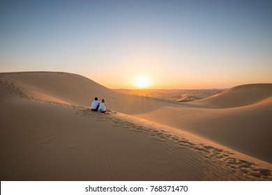 Desert landscape with young couple  looking at sunset.