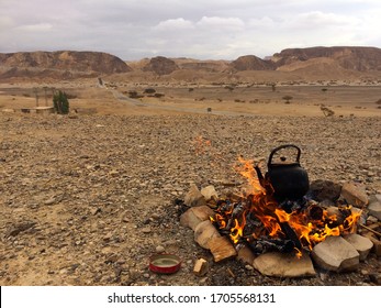 Desert open fire, roaring flames, steaming black kettle, boiling water. 