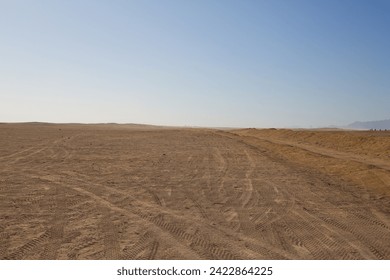 Desert road for buggy and ATV with tire tracks on the sand against the backdrop of the endless Arabian desert and clear sky - Powered by Shutterstock