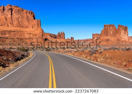 Desert Road - A sunny Winter morning view of a desert road winding towards towering red sandstone formations in Arches National Park, Utah, USA. 