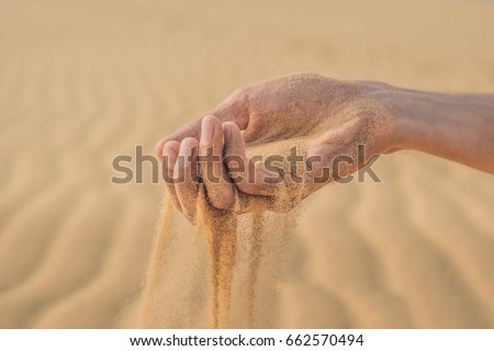 Desert, sand puffs through the fingers of a man's hand.