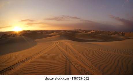 Desert at sunrise sunset hour with dune buggy tires tracks in the sand in the foreground. Buggy tour in Huacachina, Ica, Peru. Extreme sports, adventure, journey and travel concept. Wide angle shot. - Shutterstock ID 1387654052