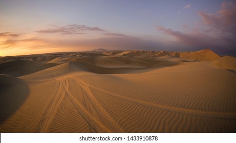 Desert at sunrise sunset hour with dune buggy tires tracks in the sand in the foreground. Buggy tour in Huacachina, Ica, Peru. Extreme sports, adventure, journey and travel concept. Wide angle shot. - Shutterstock ID 1433910878