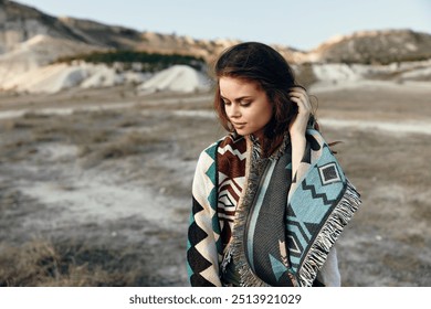 Desert wanderer woman standing with blanket over shoulders and scarf around neck in sandy landscape - Powered by Shutterstock