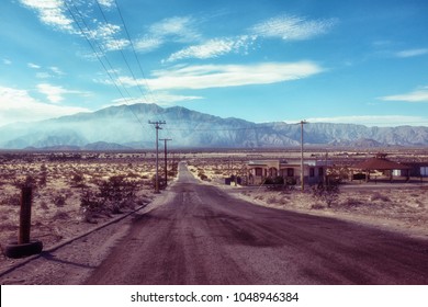 Deserted abandoned empty road in San Felipe, Mexico, South California, mountain peak in distance with blue sunny sky with few white clouds, dirty wide road and several empty houses, no people or cars - Powered by Shutterstock