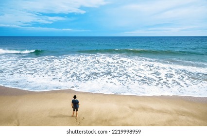 Deserted Beach And Lone Watching Man, Person Stands Alone On Sea Sand Shore, Melancholic Loner Vs Ocean, Minimal View. Concept Of Solitude, Travel, Nature, Vacation, Sadness, Freedom, Island And Mind