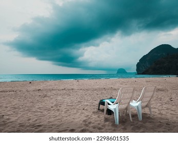 A deserted Beach in Thailand with Two White Plastic Garden Beach Chairs on the Sand as a Storm Cloud Looms in Overhead Dark Skies before it Begins tropical raining monsoon season cloudy warm paradise  - Shutterstock ID 2298601535