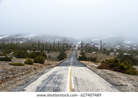 A deserted and cold road where the end is uncertain. This image contains several colorful. Foggy weather concept. There is snow in the distant mountains.