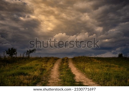 deserted country dirt road up over hilltop under evening dramatic cloudy sky.  moody summer landscape