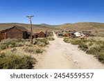 Deserted dirt street and abandoned building in the summer desert landscape environment of Bodie State Historic Park, a deserted mining ghost town in California, USA with a cloudless blue sky. 