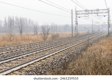 Deserted electric railway running under a motorway bridge in the countryside on a foggy winter morning - Powered by Shutterstock