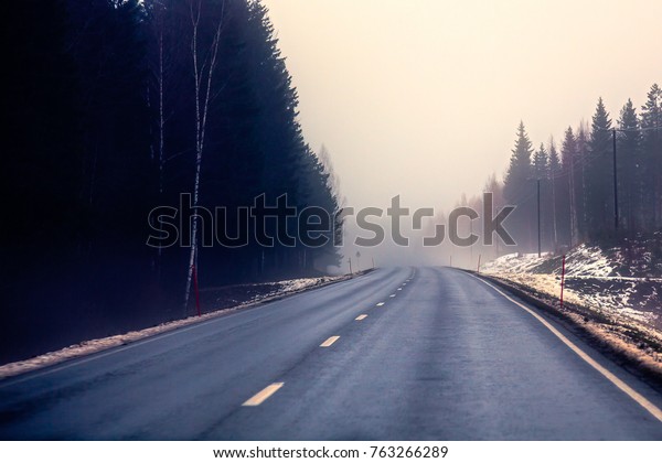 A deserted highway is in\
the fog