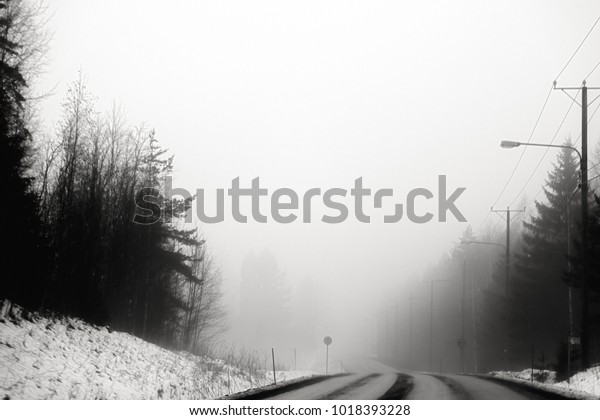 A\
deserted highway is in the fog in black and\
white