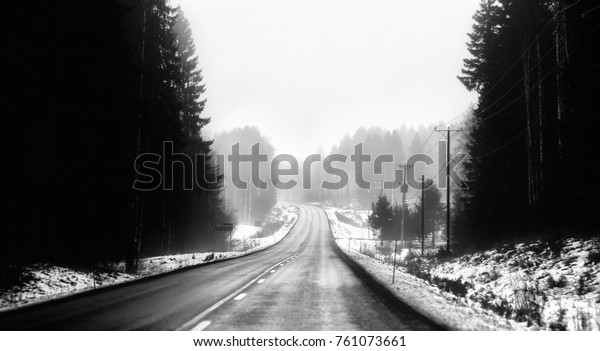 A\
deserted highway is in the fog in black and\
white