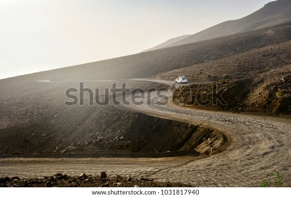 Deserted\
landscape with ground road on Jandia peninsula on Fuerteventura\
island in Spain. A white car rides along the road to the beach with\
surfboards on the roof. Canary Islands.\
