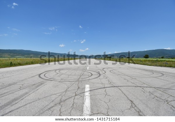 Deserted military airport runway near\
Sapareva Banya, Bulgaria, nowadays used for amateur car races,\
cracks and tire tracks seen on the old asphalt\
surface