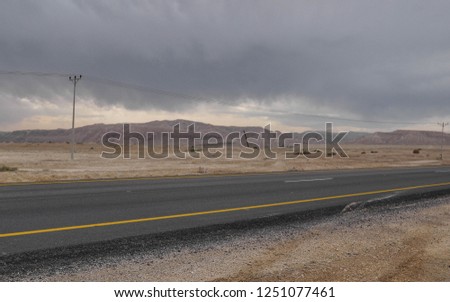 Deserted road between the mountains without people or cars on a wintery day. The picture was taken on a road trip in Israel. a few desert plants and electric poles are in sight