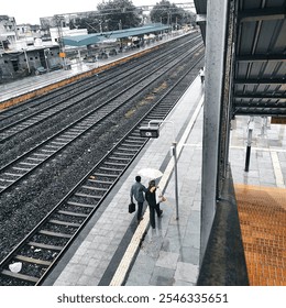 A deserted train station platform during a rainy day. Two friends with umbrellas walk along the platform. The image conveys a sense of solitude and the quietness of the station. - Powered by Shutterstock