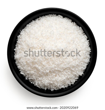 Desiccated coconut in black ceramic bowl isolated on white. Top view.