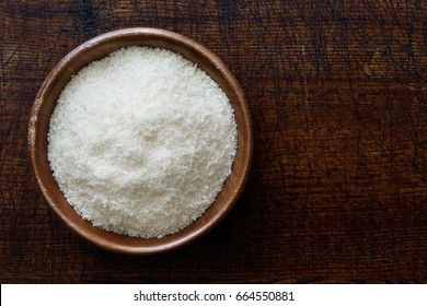 Desiccated Coconut In Dark Wooden Bowl Isolated On Dark Brown Wood From Above.
 