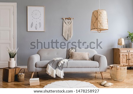 Design bohemian composition of living room interior with gray sofa, wooden cube, commode, beige macrame, rattan lamp ,plants, plaid, flowers and elegant accessories. Stylish home decor. Template.