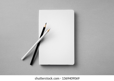 Design concept - top view of close white notebook with 2 wooden pencil on grey background for mockup. real photo, not 3D render