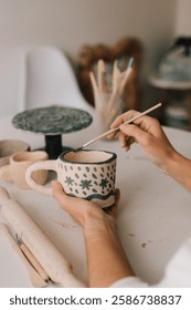 Design earthenware cup with a traditional pattern. Artist is making decoration on clay ceramic mug after oven firing
