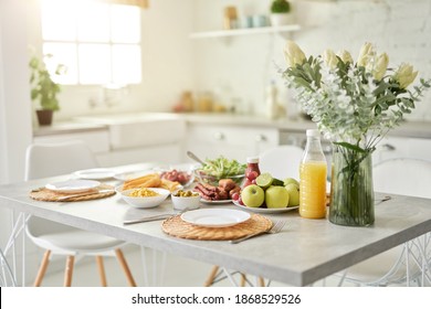 Entwerfen Sie Ideen. Nahaufnahme der Vase mit Blumen und Frühstück im lateinischen Stil auf dem Küchentisch. Moderne, helle, weiße Küche mit Holzdetails