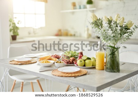 Design ideas. Close up of vase with flowers and Latin style breakfast on the kitchen table. Modern bright white kitchen interior with wooden and white details