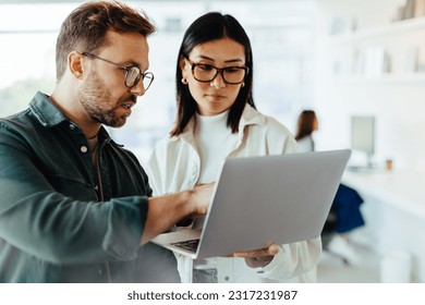 Design professionals standing in an office and using a laptop together. Two young business people discussing a project.