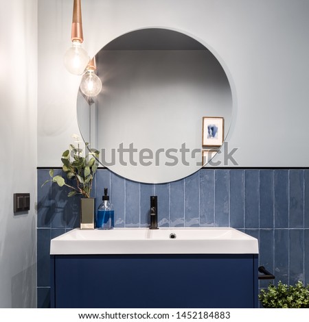 Designed bathroom with stylish blue cabinet, blue wall tiles and big round mirror