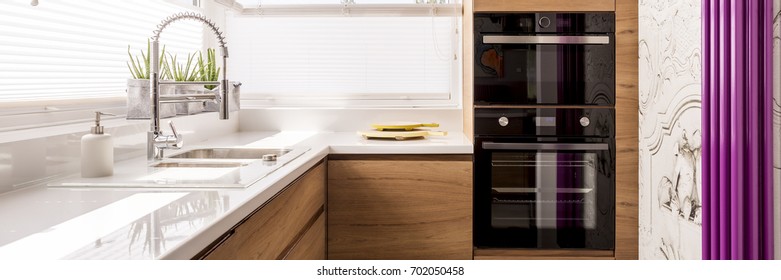 Designed Kitchen With White Glossy Countertop And Stainless Steel Faucet In Front Of Violet Heater