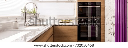 Designed kitchen with white glossy countertop and stainless steel faucet in front of violet heater