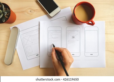 Designer Drawing Mobile Application Wireframe On Wooden Desk. Top View