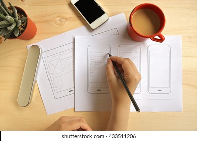Designer drawing mobile application wireframe on wooden desk. Flat lay - Shutterstock ID 433511206