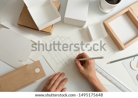 Designer draws a mockup for crafting eco cardboard box. Development a sketch of paper packaging.