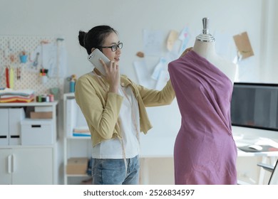 Designer girl wearing glasses Talking on the phone and examining the design of the clothes on the mannequin While doing a set of fashionable clothes - Powered by Shutterstock