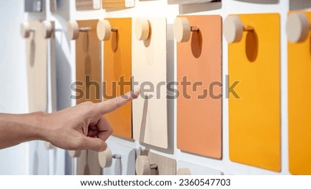 Designer hand pointing at colorful laminate sheet on material swatch wall display in material library. Choosing color board from collection for interior architecture and furniture finishing design