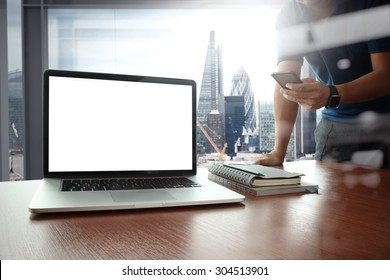 designer hand working and smart phone and blank screen laptop on wooden desk in office with london city background