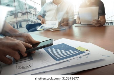 Designer Hand Working And Smart Phone And Laptop On Wooden Desk In Office And Two Colleagues Discussing Data With London City Background

