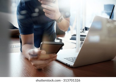 Designer Hand Working And Smart Phone And Laptop On Wooden Desk In Office And Two Colleagues Discussing Data With London City Background