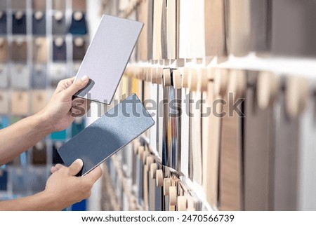 Designer hands compare two gray laminate sheets nearby material swatch wall display in material library. Choosing color board from collection for interior architecture and furniture finishing design