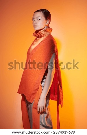 Designer knitwear. Stylish fashion model posing in wide leg trousers and a knitted poncho in studio in mixed color light. Bright colors. New fashionable demi-season collection. 
