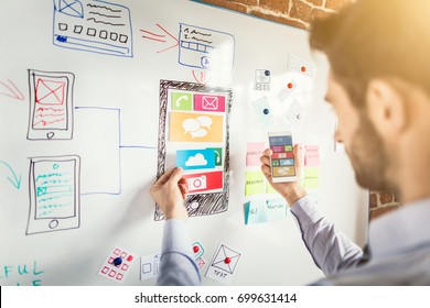 Designer man drawing website ux app development and holding smart phone on hand. User experience concept.