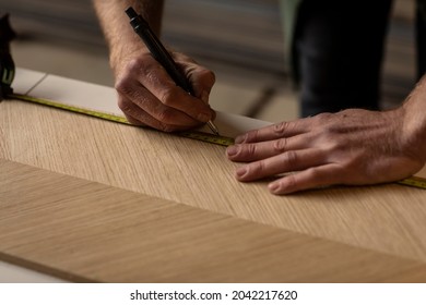 A designer man using his measuring tape to measure a piece of veneer wood and making furniture in his carpentry workshop studio  - Powered by Shutterstock