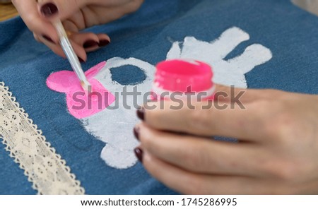 Designer painting an angel on denim cloth. He creating his personal collection dresses for girls