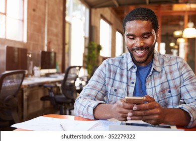Designer Sitting At Meeting Table Texting On Mobile Phone