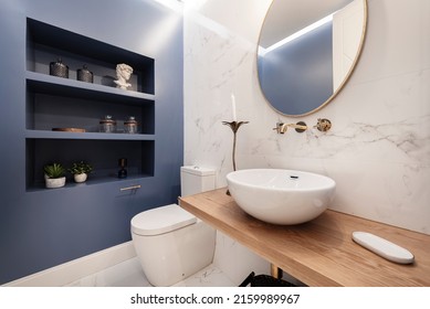 Designer Toilet With Half Circle Porcelain Sink On Light Wood Countertop And Ornate Shelving On Blue Wall