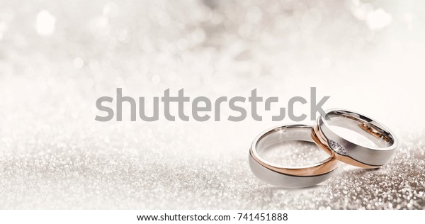 Designer wedding rings in the corner on a sparkling\
glitter background in panoramic banner format with copy space and\
selective focus